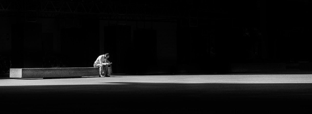 grayscale photogaphy of man sitting on concrete bench